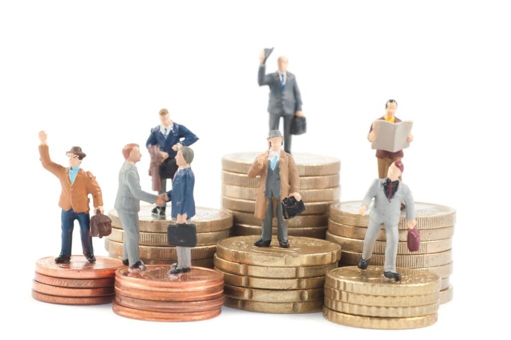 Miniaturas de pessoas em cima de pilhas de moedas de diferentes valores.