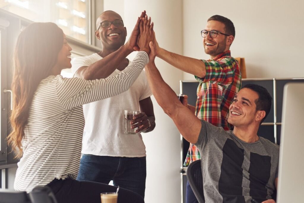 Quatro empreendedores de diversas etnias se reúnem para um high-five, celebrando um sucesso de equipe e a colaboração no ambiente de trabalho.