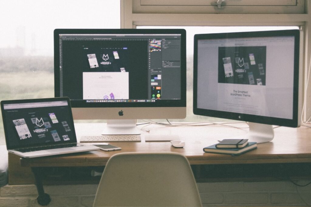 Espaço de trabalho remoto com dois monitores, um laptop e materiais de design.