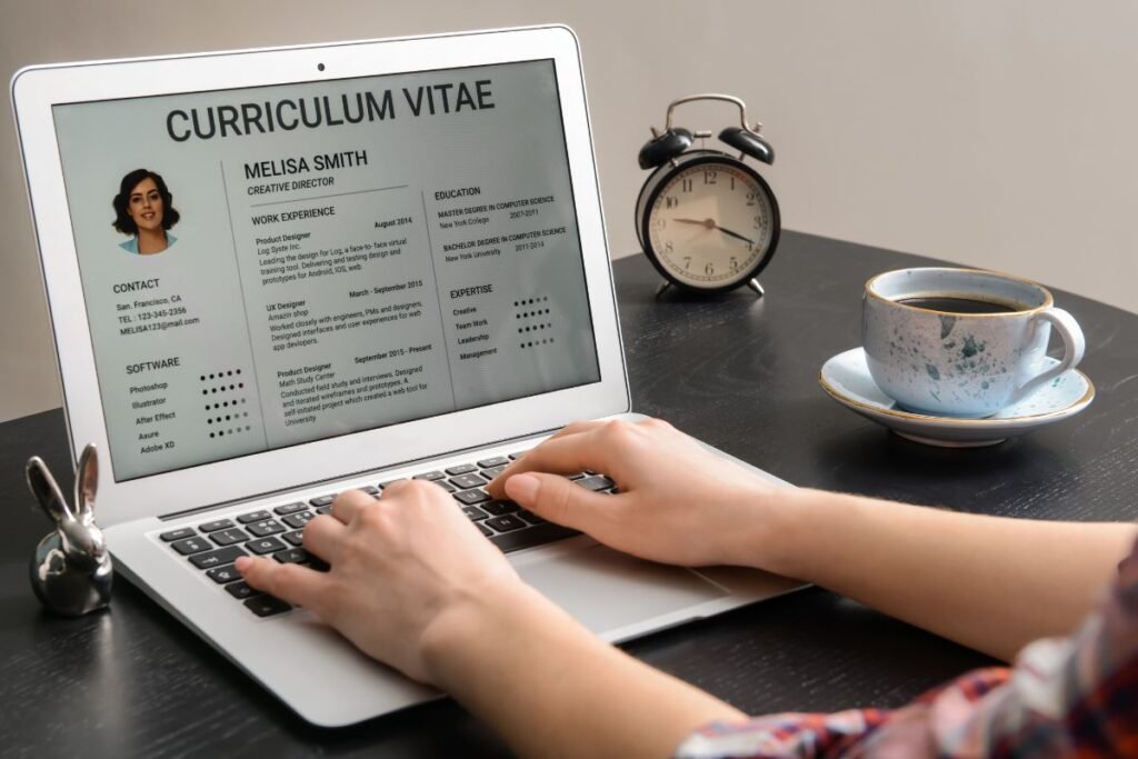 Uma pessoa digitando em um laptop que exibe um currículo (Curriculum Vitae) de "Melisa Smith" na tela. Ao lado, há um despertador e uma xícara de café.