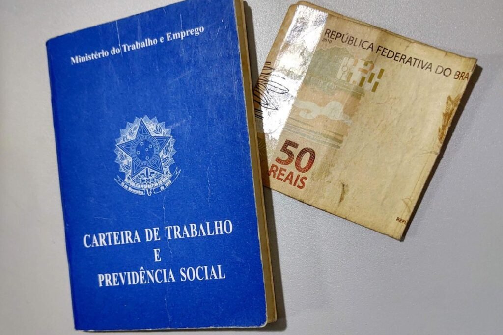 Carteira de Trabalho e Previdência Social ao lado de uma nota de cinquenta reais, simbolizando o 13º salário.