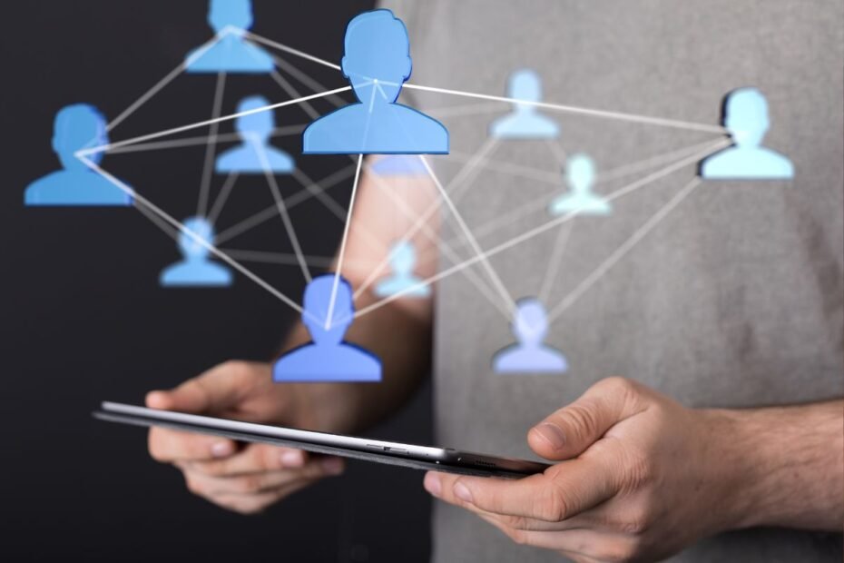 Uma pessoa segurando um tablet, com uma projeção digital de ícones de pessoas azuis conectadas por linhas, ilustrando o uso da tecnologia para networking.
