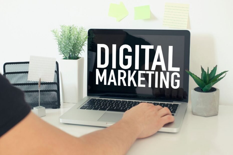 Tela de laptop mostrando as palavras "DIGITAL MARKETING" em um escritório doméstico moderno.