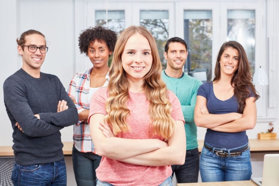 Grupo diversificado e sorridente de jovens profissionais e aprendizes posando com confiança em um ambiente de trabalho moderno.